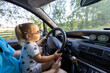 A cute little girl driving a car on her father's lap. Child girl in sunglasses with a serious expression learns to steer a car. A father teaches his daughter how to drive a car.