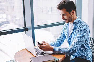 Wall Mural - concentrated male freelancer sharing information via smartphone and laptop