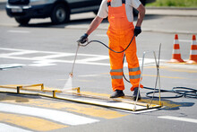 Worker painting zebra crossing stripes with spray gun. Road surface marking, painting and remarking pedestrian crosswalk. Worker use paint sprayer, applies white marking to striped crosswalk