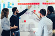 © BullRun - Young multiethnic business partners having discussion while analyzing wall with sticky notes at office
