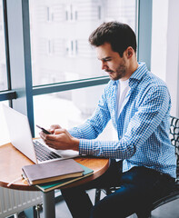Wall Mural - concentrated male freelancer sharing information via smartphone and laptop