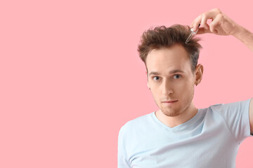 Wall Mural - Young man using serum for hair growth on pink background