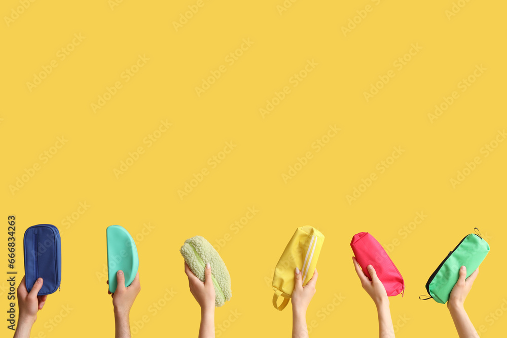 Hands with pencil cases on yellow background
