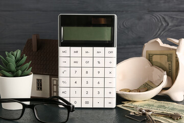 Wall Mural - Calculator, broken piggy bank, money and house model on black table