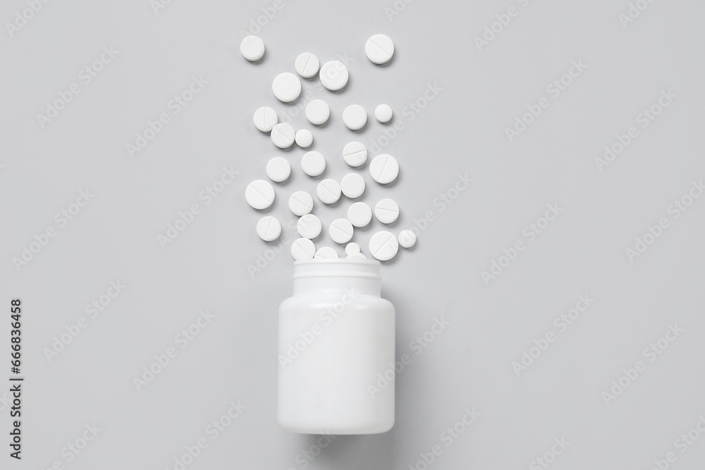 Jar with scattered pills on grey background