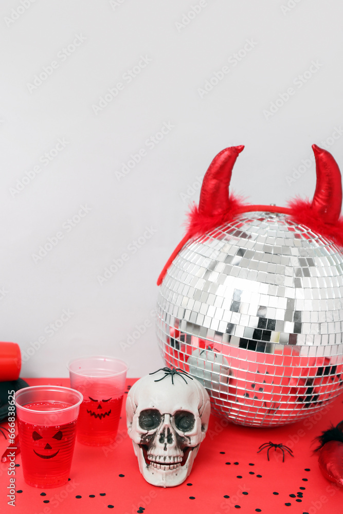 Halloween party composition with punch, skull and disco ball on red table against white background