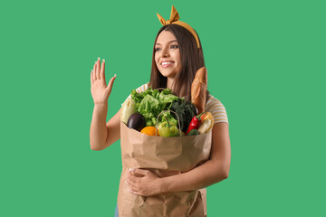 Sticker - Young woman holding paper bag with fresh vegetables on green background