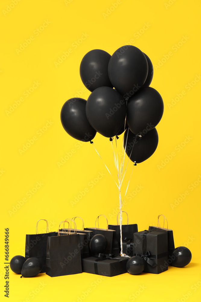 Gift boxes with balloons and shopping bags on yellow background. Black Friday sale