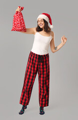 Canvas Print - Beautiful young woman in pajamas with Santa Claus bag on grey background