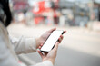 © bongkarn - Close-up image of a woman using her smartphone while walking down the street in the city.
