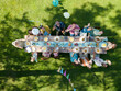Top view of people at summer garden party in beautiful garden. BBQ family gathering, with a set table and colorful decorations. Family waving up.