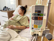 automatic infusion IV drip saline pump machine with pregnant woman resting on bed in hospital