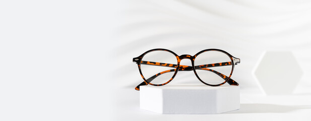 Canvas Print - Glasses sale banner. Optic store sale-out offer. Trendy tortoiseshell frame glasses on a podium on white background. Copy space for text. For banner, web line. Optic store discount, eyewear promotion