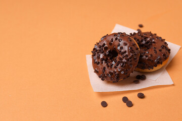 Wall Mural - Chocolate donuts on paper on orange background, space for text