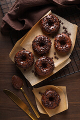 Wall Mural - Chocolate donuts on paper, towel and cutlery on wooden background, top view