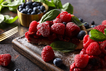 Wall Mural - Pieces of berry pie on kitchen board, bowl with berries and basil on dark gray background, close up