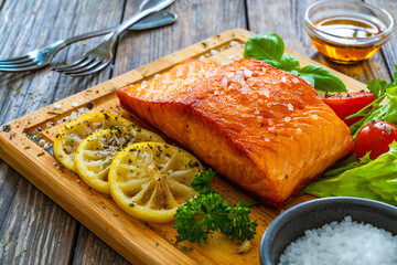 Seared salmon steak with lettuce, tomatoes and lemon on wooden table
