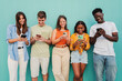 © Jose Calsina - Multiracial group of young friends enjoying and smiling using their mobile phone app at teal wall. Teenagers having fun sharing messages on social media with a cellphone at blue color background. High
