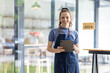 © David - Startup successful small business owner sme beauty girl stand with tablet smartphone in coffee shop restaurant. Portrait of asian tan woman barista cafe owner. SME entrepreneur seller business concept