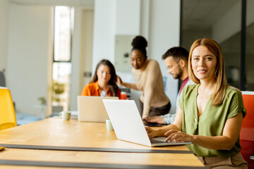 Wall Mural - Business woman working on laptop with her young multiethnic startup team working in the modern office