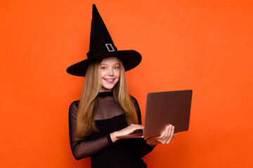 Canvas Print - Photo of shiny adorable girl dressed dark witch dress headwear communicating modern device isolated orange color background