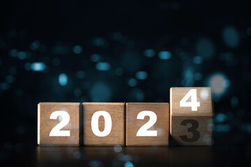 Wall Mural - flipping of 2023 to 2024 on wooden block cube with dark background and bokeh for preparation new yea