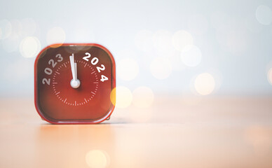 Wall Mural - 2023 and 2024 on red alarm clock on wooden table with copy space and bokeh , merry christmas and hap