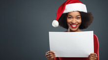 Happy African American Woman Holding Blank Card With Santa Claus Hat On Grey Studio Background. Christmas Celebration