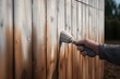A person holding a brush near a wooden fence. This image can be used to depict activities such as painting, maintenance, or DIY projects involving fences