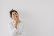 Asian Thai Woman Wear Sweater Bun Hair, Touching Chin And Mouth With Doubt And Curious Face, Have Question Thinking And Looking At Empty Space, Isolated On White Background Wall At Winter.