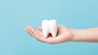 Hand holding a tooth close-up on a blue background with copyspace. Dental clinic concept for dental treatment