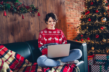 Photo of pretty young girl sit sofa working remotely netbook wear trendy red sweater festive interior living room presents christmas tree