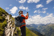 © Guzel - Gray-haired male climber with backpack standing on steep trail and taking pictures of valley, Austria