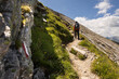 © Guzel - Sporty man with backpack climbing a trail uphill against the background of rocks and sky with clouds, Austria