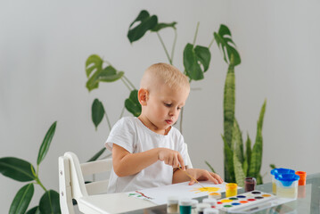 a handsome boy painting with a paintbrush and writing on paper sitting at home at his desk