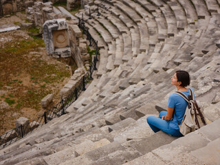 Wall Mural - Woman tourist sitting in amphitheater enjoying solitude. travel to ancient city of Side, Antalya coast of Turkey in tourist low season. view of ancient theatre or Amphitheatre in Side, Turkey.