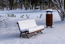   snow-covered bench and rubbish bin in the park