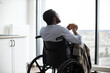 © sofiko14 - Back view of african american wheelchair user with cup of hot drink looking at panoramic window resting in open-plan kitchen of modern apartment.