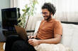© Fxquadro - Happy male student working on a laptop while seated on a couch in a cozy room