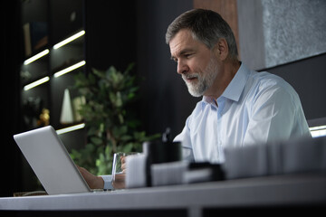 Wall Mural - Businessman using laptop computer in office. Happy mature aged man, entrepreneur, small business owner working online.