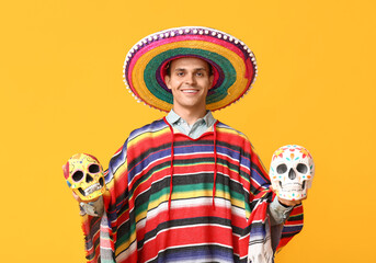 Wall Mural - Handsome young man in sombrero with painted skulls on yellow background