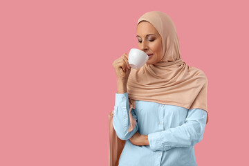 Poster - Mature Muslim woman in hijab with cup of coffee on pink background