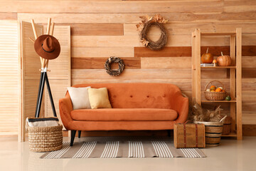 Interior of living room with brown sofa, rack, wreathes and pumpkins on shelving unit