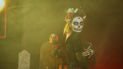 Wall Mural - Glamorous woman with sugar skull make up and flowers headband, dressed in goddess of death costume as santa muerte. Dios de los muertos art to celebrate mexican tradition in studio. Handheld shot.