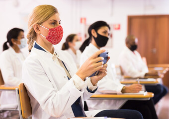 Canvas Print - Focused woman in protective face mask attending medical seminar, using smartphone to record lecturer speech. Precautions during coronavirus pandemic..