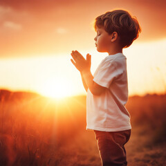 child praying  with hands together, at sunset in the field outdoors in a summer day