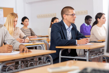 Wall Mural - Portrait of focused male sitting at desk studying in classroom with colleagues