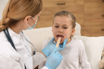 Canvas Print - Doctor in medical mask examining girl`s oral cavity with tongue depressor indoors