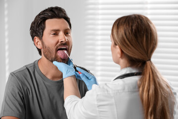 Canvas Print - Doctor taking throat swab sample from man`s oral cavity indoors