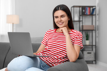 Poster - Happy young woman having video chat via laptop on sofa in living room